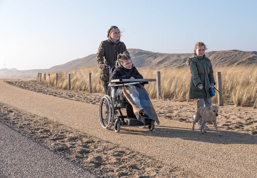 Meisje in rolstoel wandelt met moeder, zusje en hond door de duinen