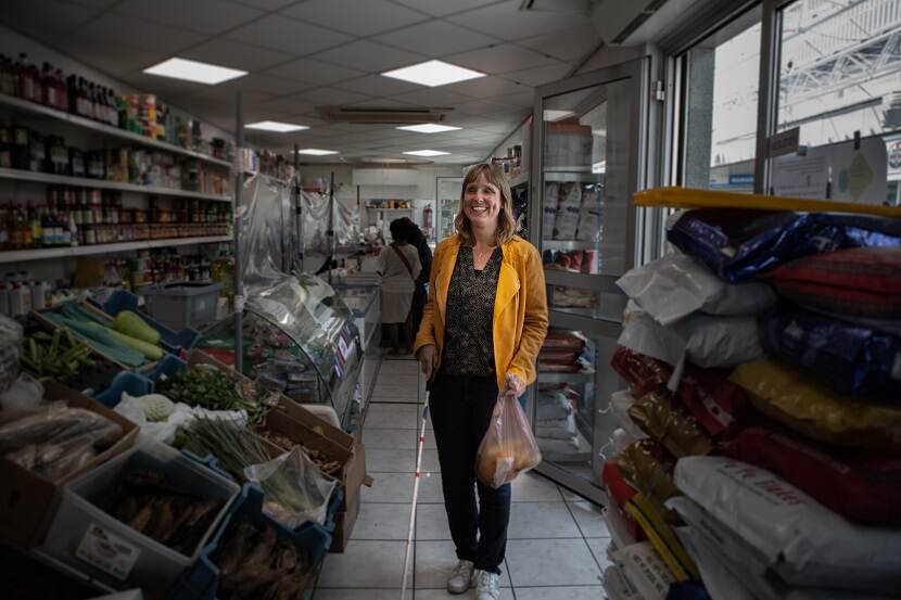 Een vrouw met een visuele beperking met een geleidestok staat in een lokale supermarkt