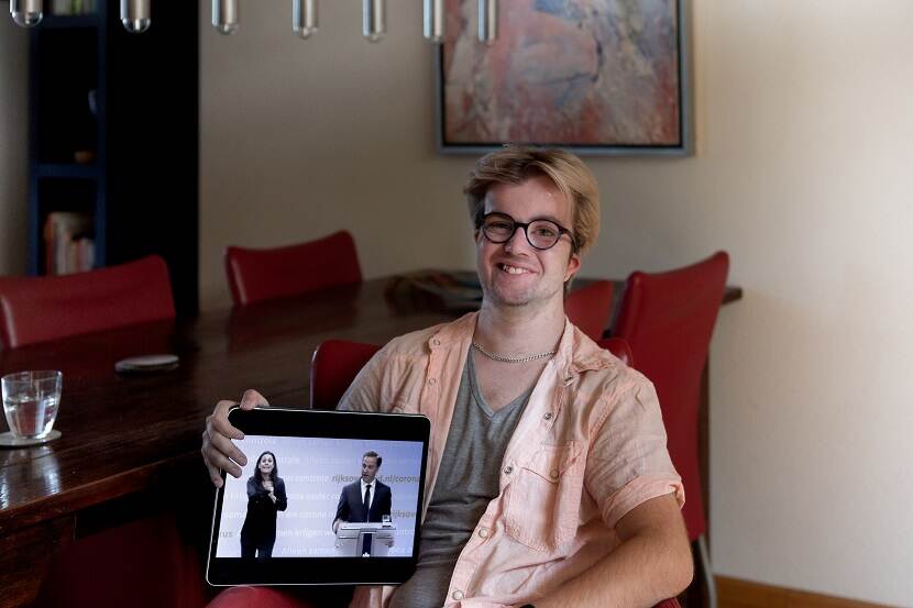 Portretfoto van de slechthorende Tom met een tablet op zijn schoot waarop een van de persconferenties over het coronavirus wordt afgespeeld met een Nederlandse Gebarentolk